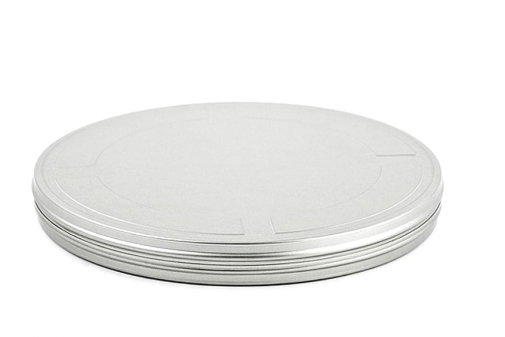 Geschlossene runde Filmdose aus silberfarbenem Metall mit flachem Stülpdeckel, auf weißem Hintergrund fotografiert.