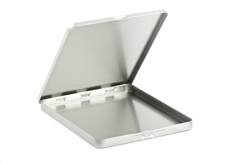Geöffnete eckige Metalldose aus silberfarbenem Blech mit aufklappbarem Deckel und sichtbarem Scharnier, fotografiert vor weißem Hintergrund.